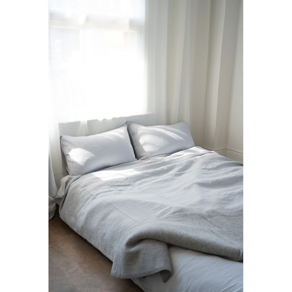 Neatly made bed with light gray bedding in a bright room.