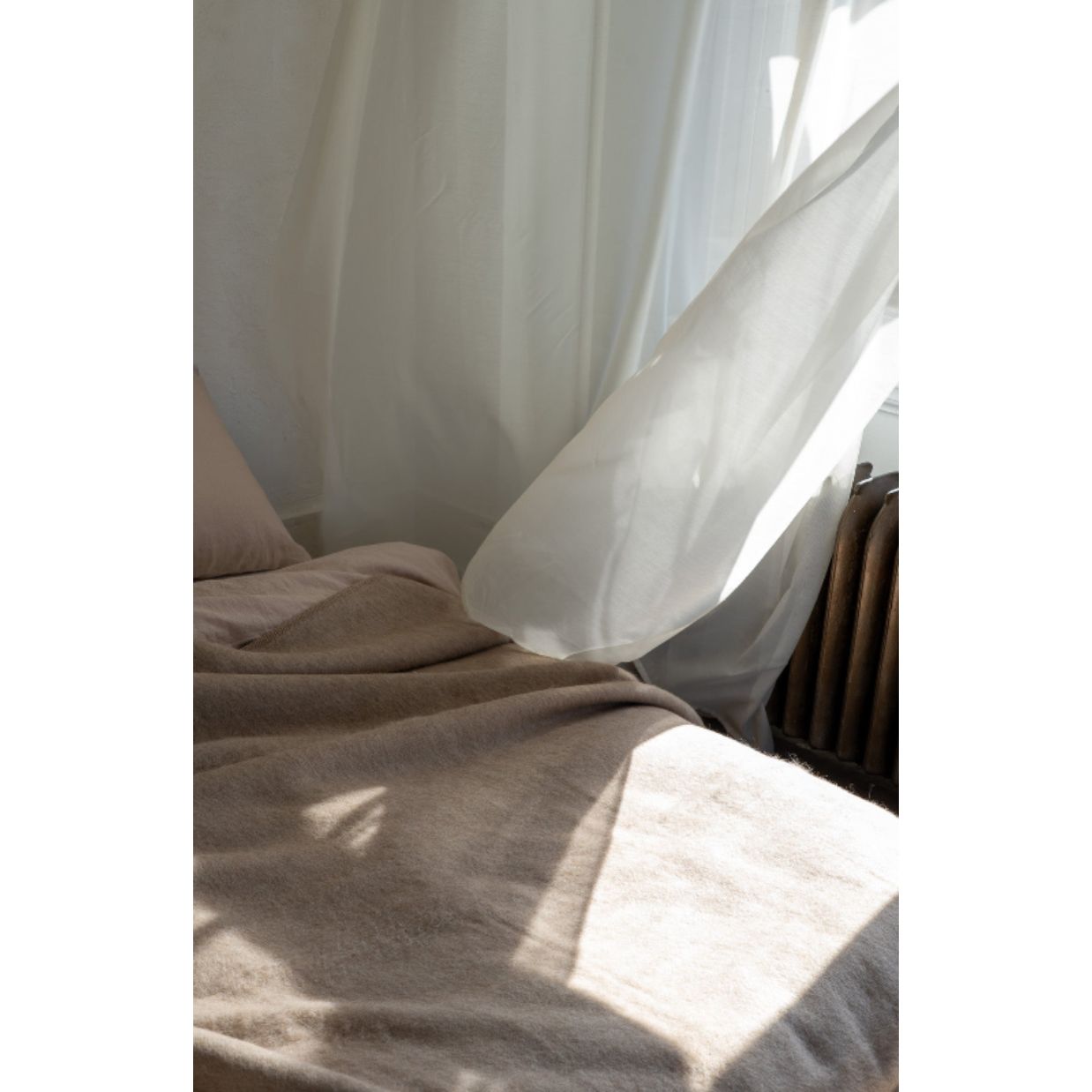 Light filtering through sheer curtains on a bed with brown bedding.