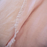 A close-up of a soft blush pink fabric with a fringed edge, draped to show its texture and color.