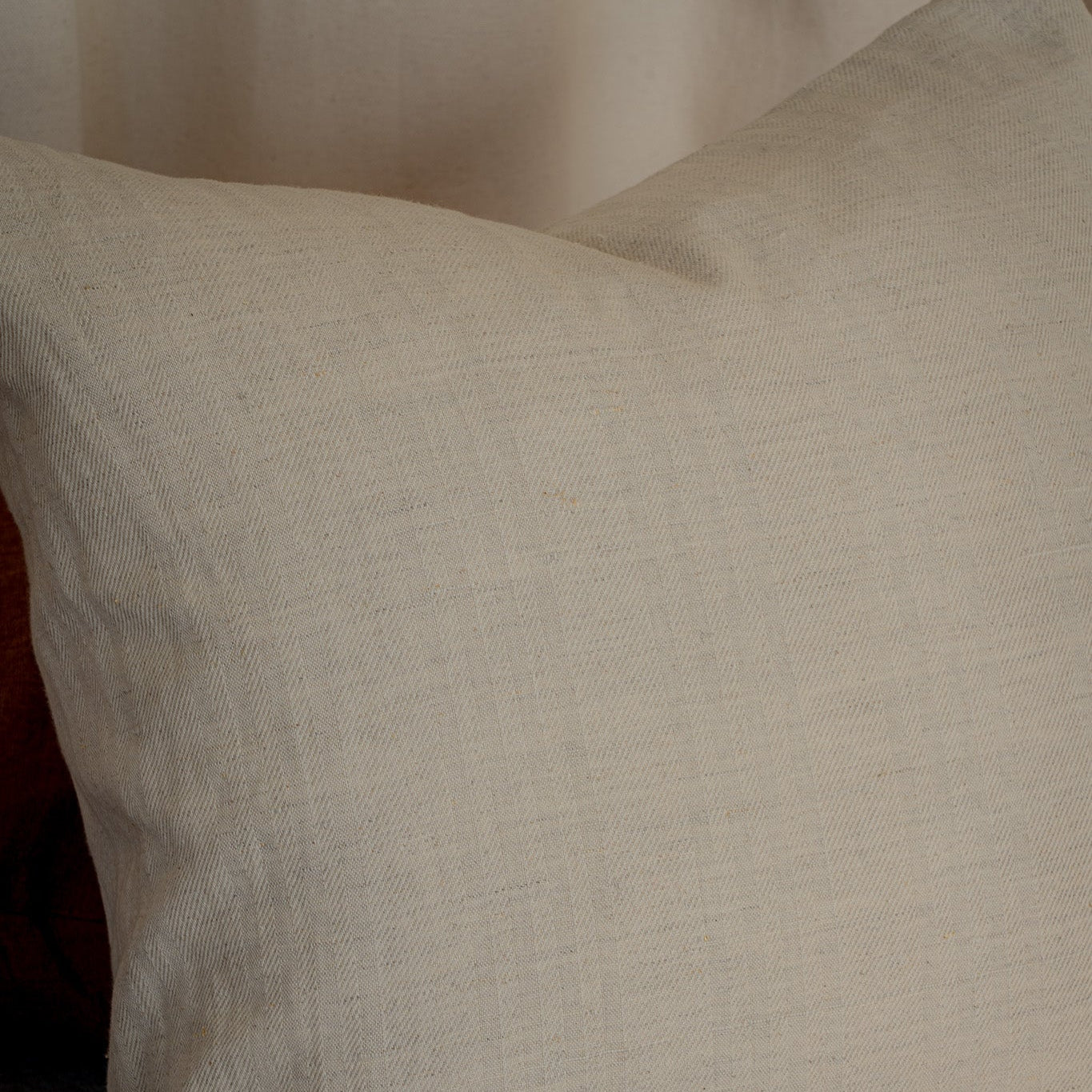 A square off-white linen throw pillow with a textured, natural woven fabric, resting on a neutral gray surface against a soft beige background.