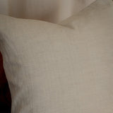 A square off-white linen throw pillow with a textured, natural woven fabric, resting on a neutral gray surface against a soft beige background.