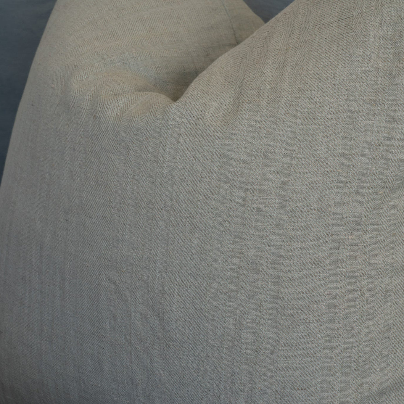 A close-up of a textured linen throw pillow in a light beige color, resting on a gray sofa.
