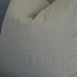 A close-up of a textured linen throw pillow in a light beige color, resting on a gray sofa.