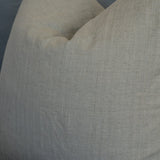 A close-up of a textured linen throw pillow in a light beige color, resting on a gray sofa.