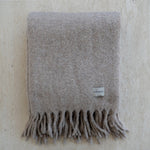 Gray blanket with fringes and a visible brand label on a textured beige background