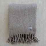 Gray blanket with fringes and a visible brand label on a textured beige background