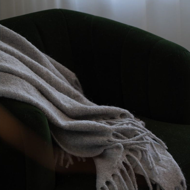 Dark green armchair with a beige blanket draped over it against a neutral background