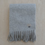 Gray blanket with fringes and a brand tag on a beige background