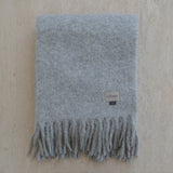 Gray blanket with fringes and a brand tag on a beige background