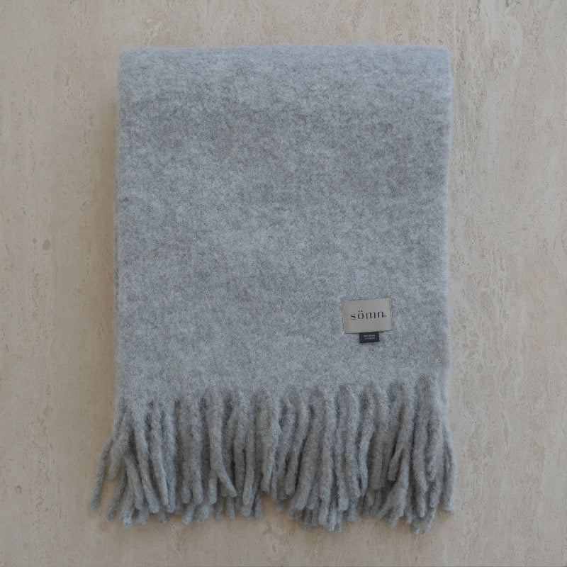 Gray blanket with fringes and a brand tag on a beige background