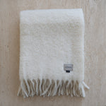 White blanket with fringes and a brand label on a beige background