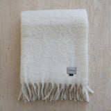 White blanket with fringes and a brand label on a beige background