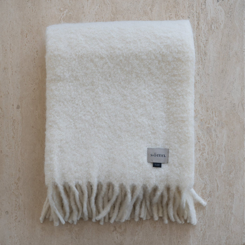 White blanket with fringes and a brand label on a beige background