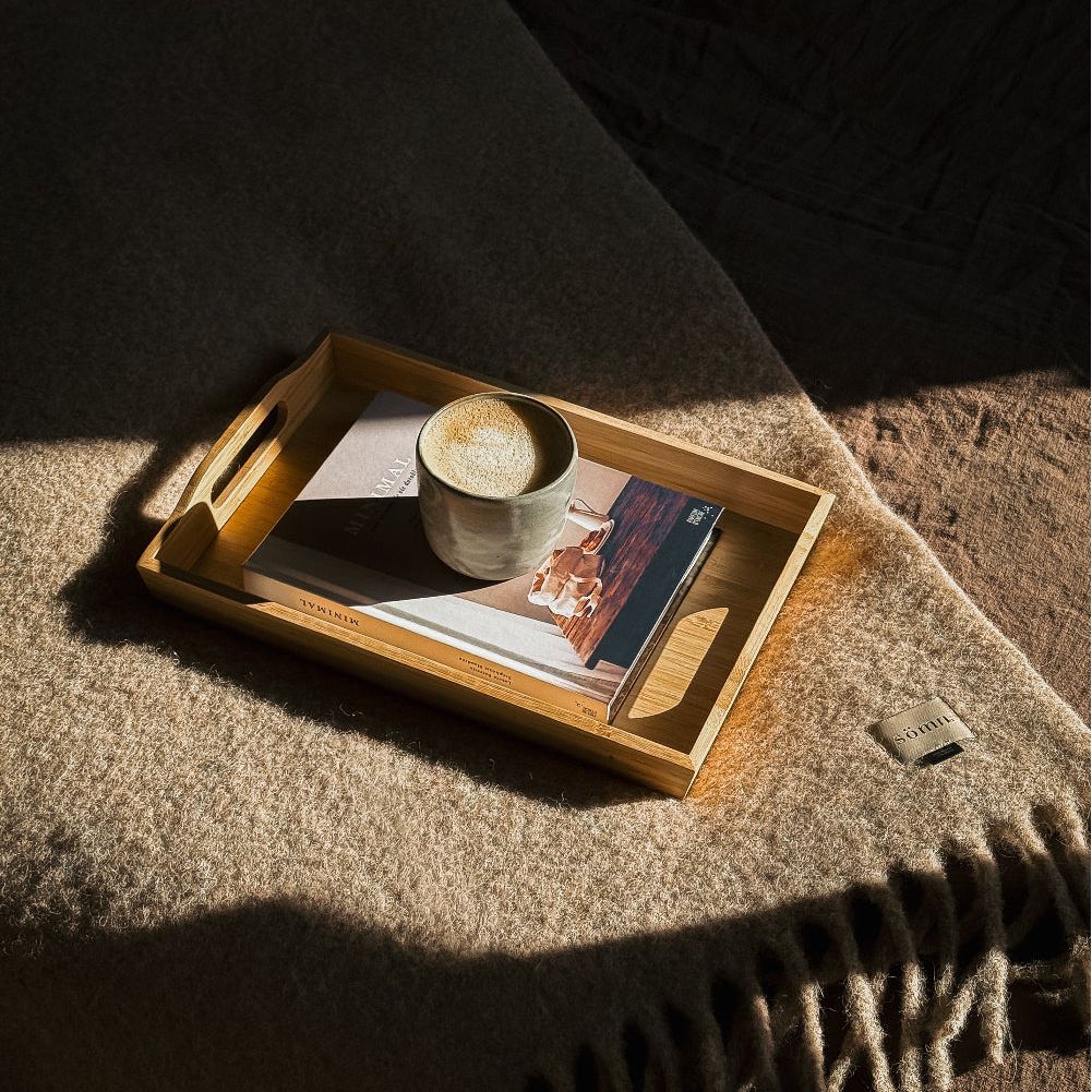 Wooden tray with a cup of coffee and book on a textured surface