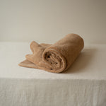 Rolled beige towel on a white surface with a neutral background