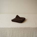 Folded brown towel on a white surface with a neutral background