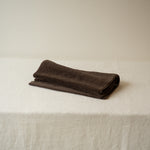 Folded brown towel on a white surface with a beige background