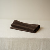 Folded brown towel on a white surface with a beige background