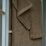 Brown towel hanging on a wooden rack against a neutral background