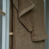 Brown towel hanging on a wooden rack against a neutral background