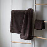 Brown towel hanging on a wooden rack against a white wall.