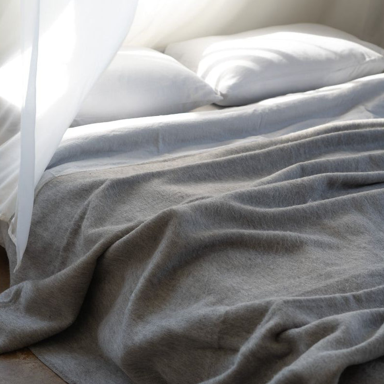 Gray blanket draped over a bed with white pillows in a softly lit room.