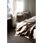 Cozy bedroom with a bed covered in brown blankets and pillows, draped over a window seat.