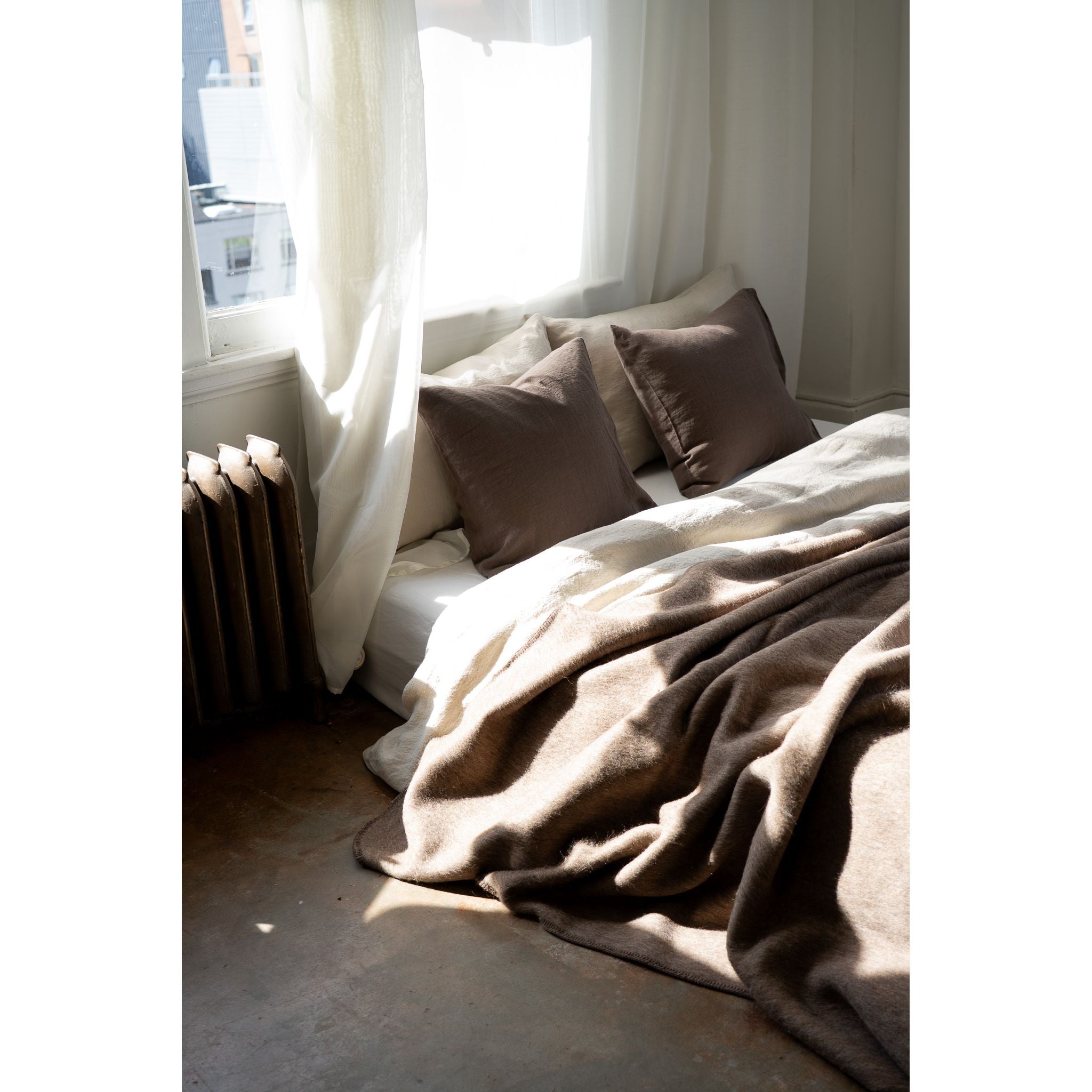 Cozy bedroom with a bed covered in brown blankets and pillows, draped over a window seat.