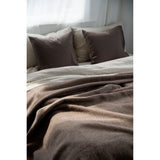 Brown bedding with pillows on a bed in a softly lit room