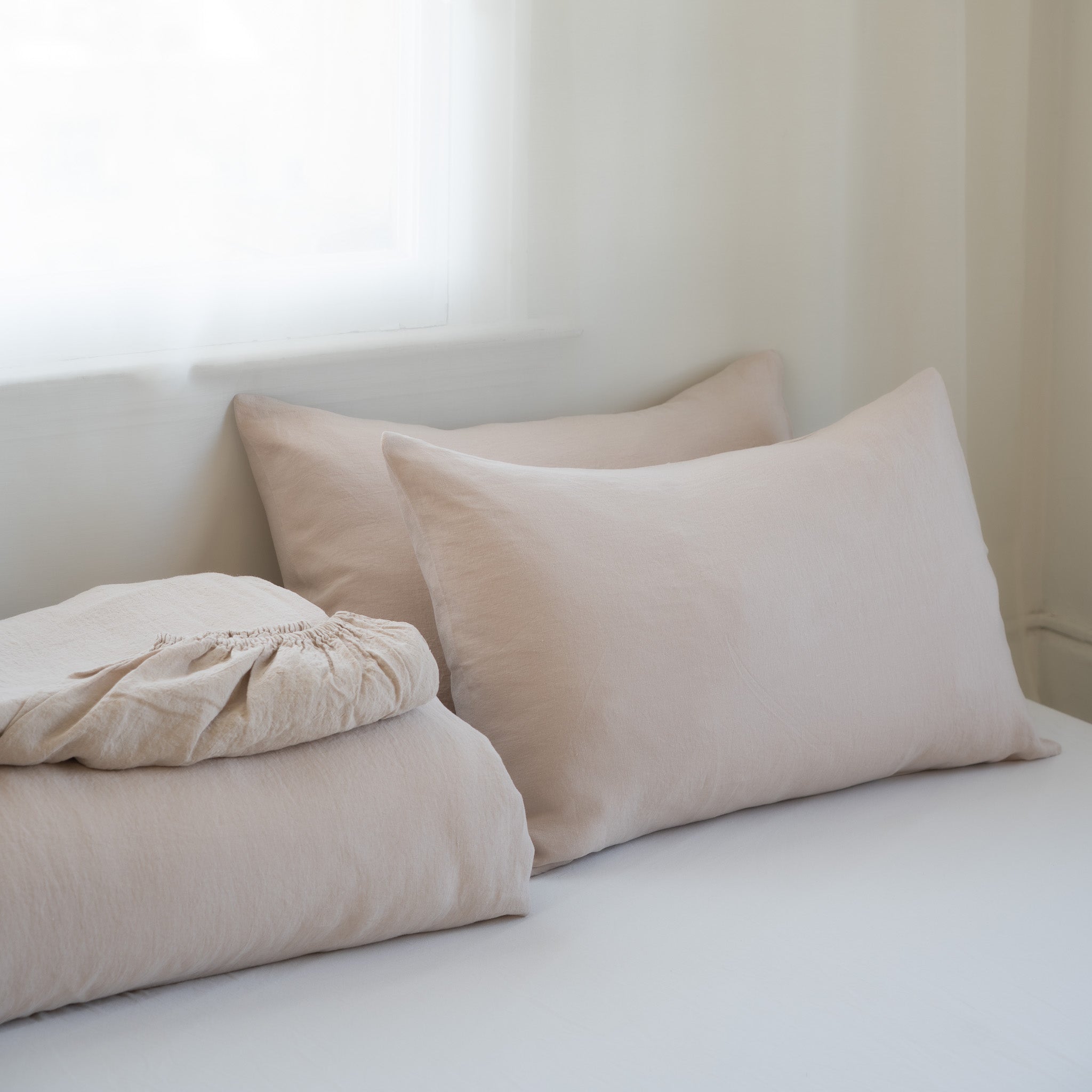Beige pillows and bed sheets on a white bed with a neutral background