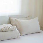 Neatly arranged pillows and a folded blanket on a bed in a softly lit room.