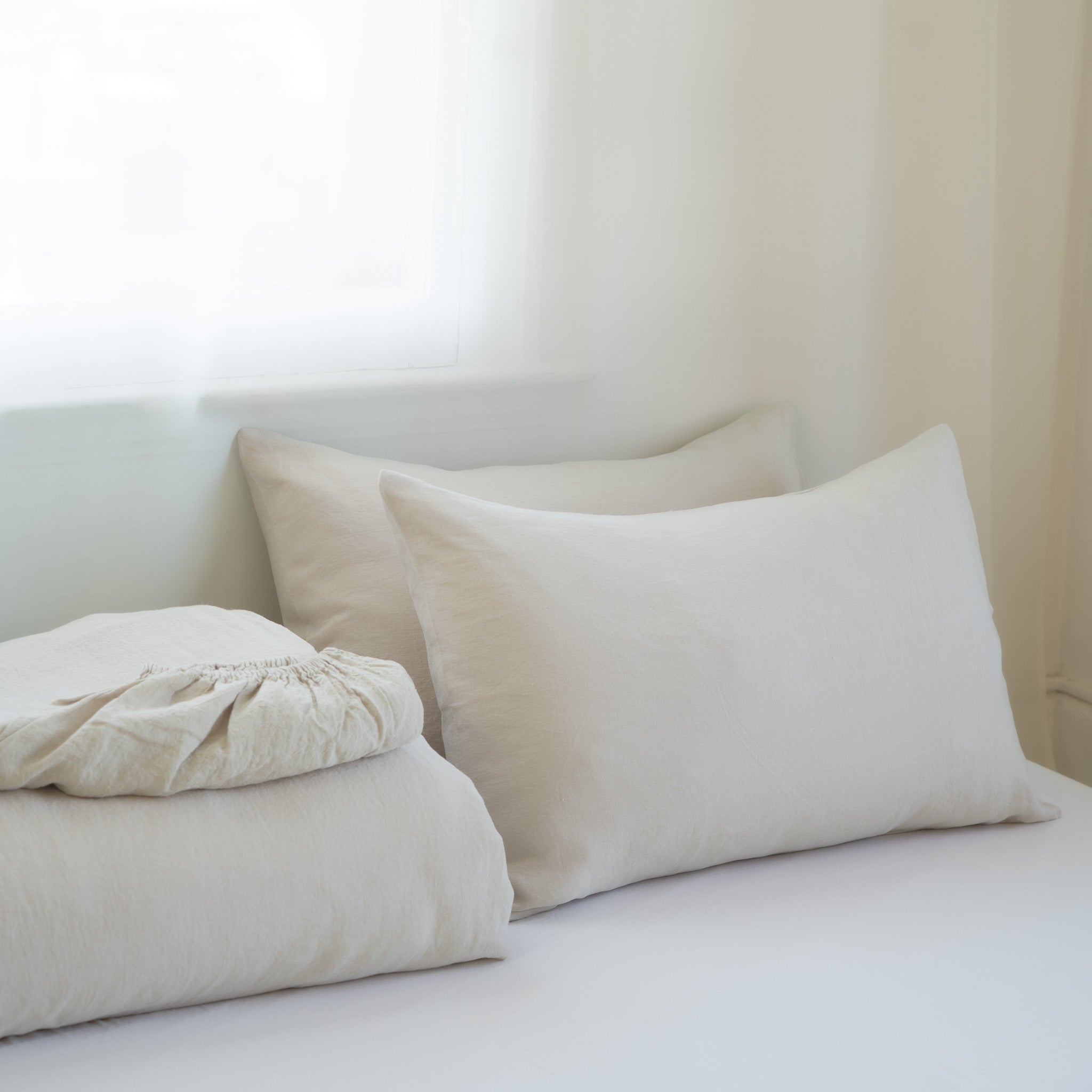 Neatly arranged pillows and a folded blanket on a bed in a softly lit room.