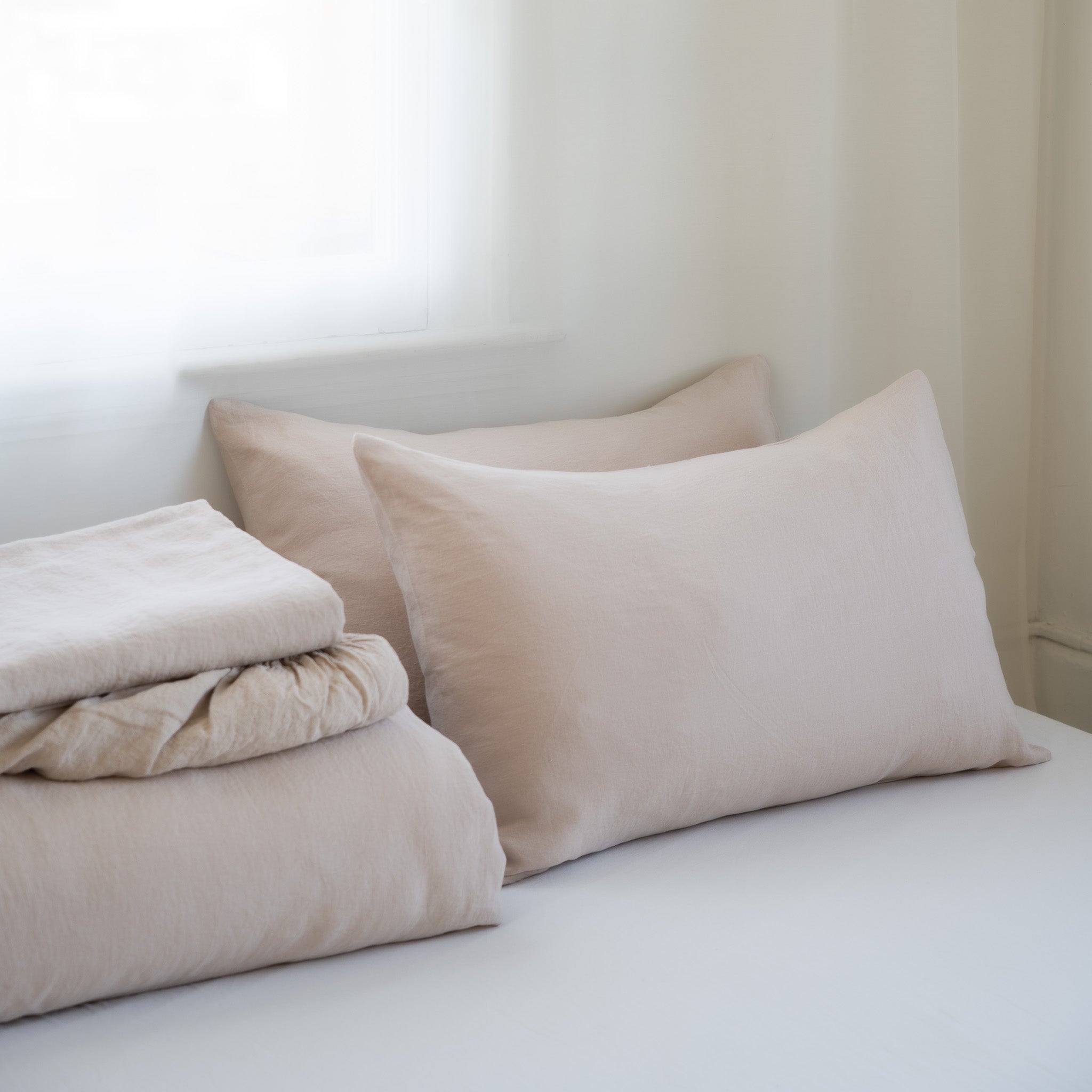 Beige folded towels and pillows on a white bed