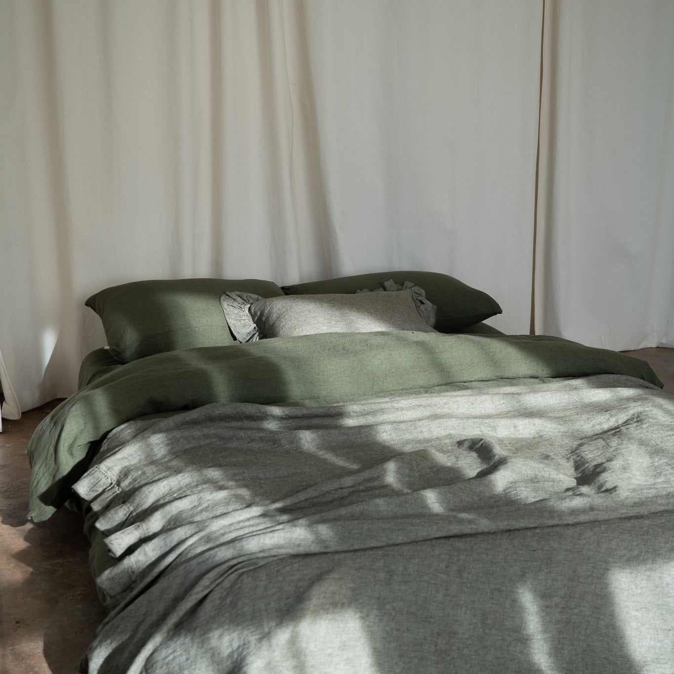 Bed with green bedding and pillows against a white curtain backdrop