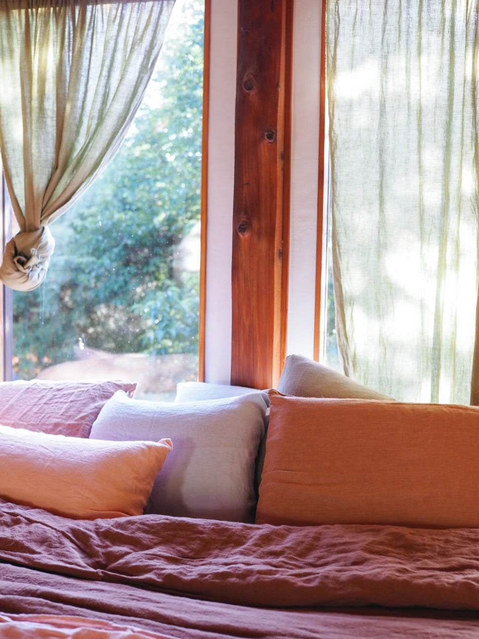 Bed with colorful bedding and pillows in a room with large windows and curtains.