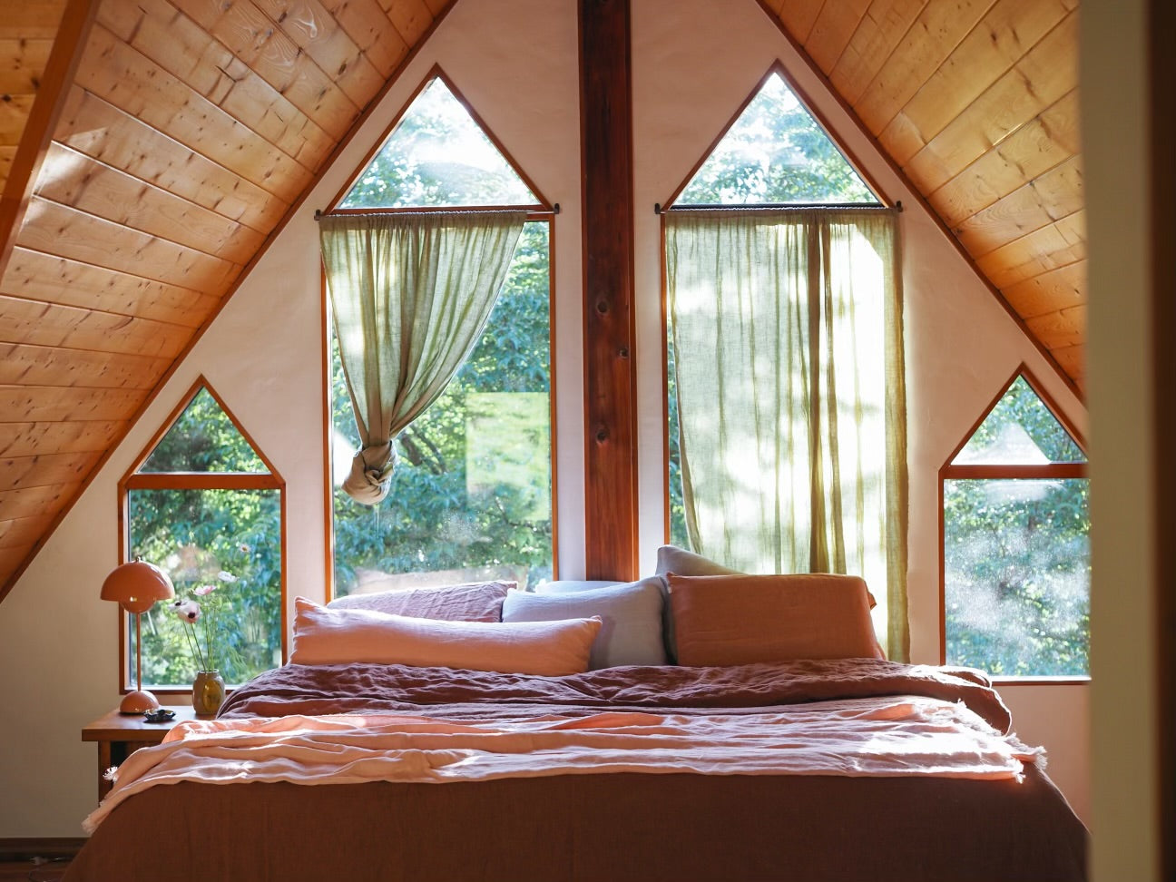 Bedroom with wooden walls and large windows showing greenery outside