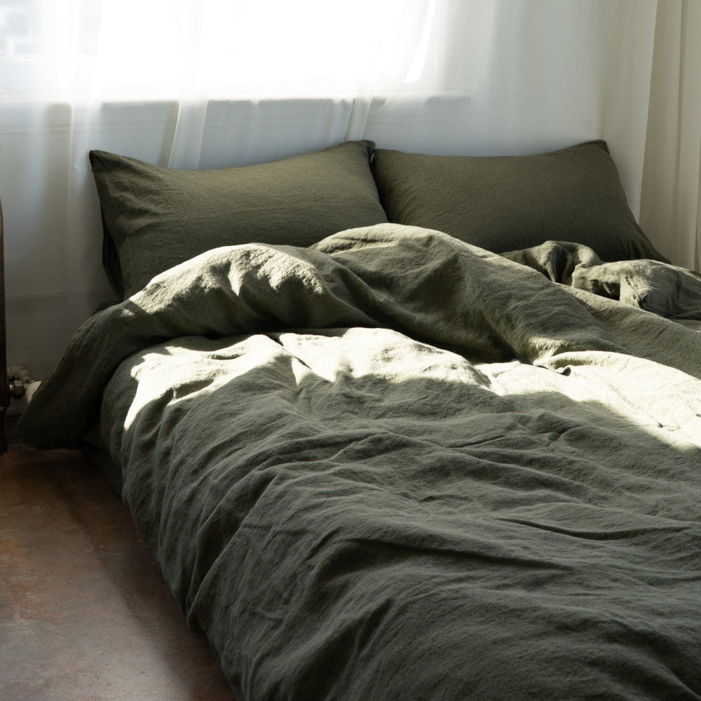 Bed with green bedding and pillows against a white curtain backdrop