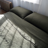 Bed with olive green bedding and pillows in a room with a radiator and window.
