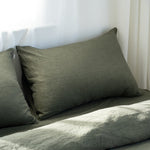 Two green pillows on a bed with a white curtain in the background