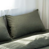 Two green pillows on a bed with a white curtain in the background