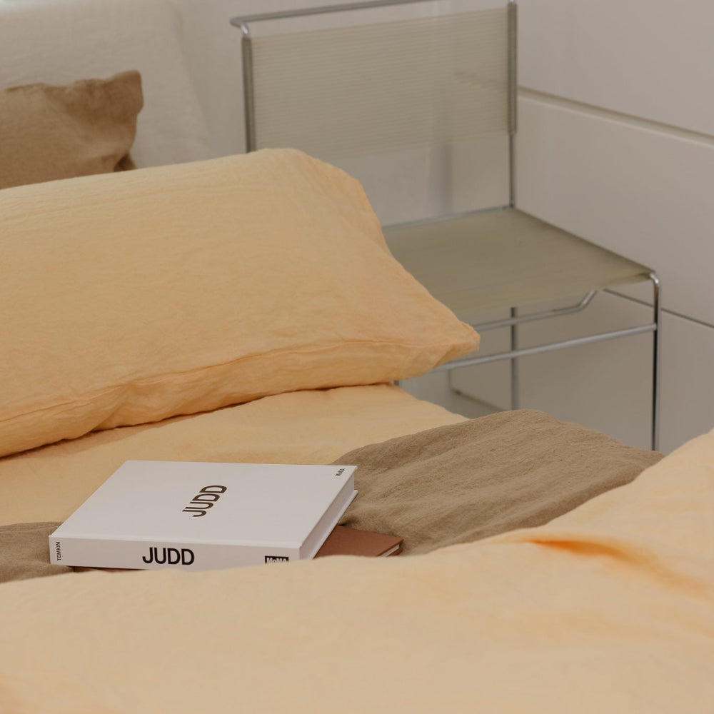 Book titled 'JUDD' on a bed with peach bedding and a chair in the background.