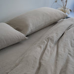 Beige bedding set with two pillows on a bed against a light blue wall.