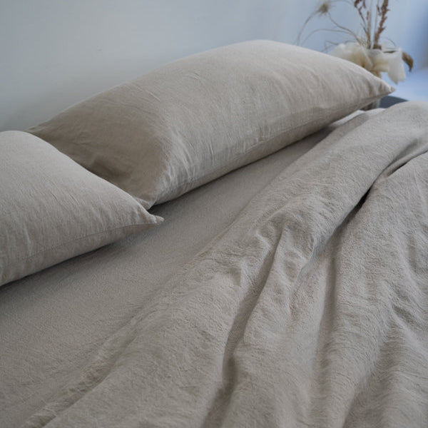 Beige bedding set with two pillows on a bed against a light blue wall.