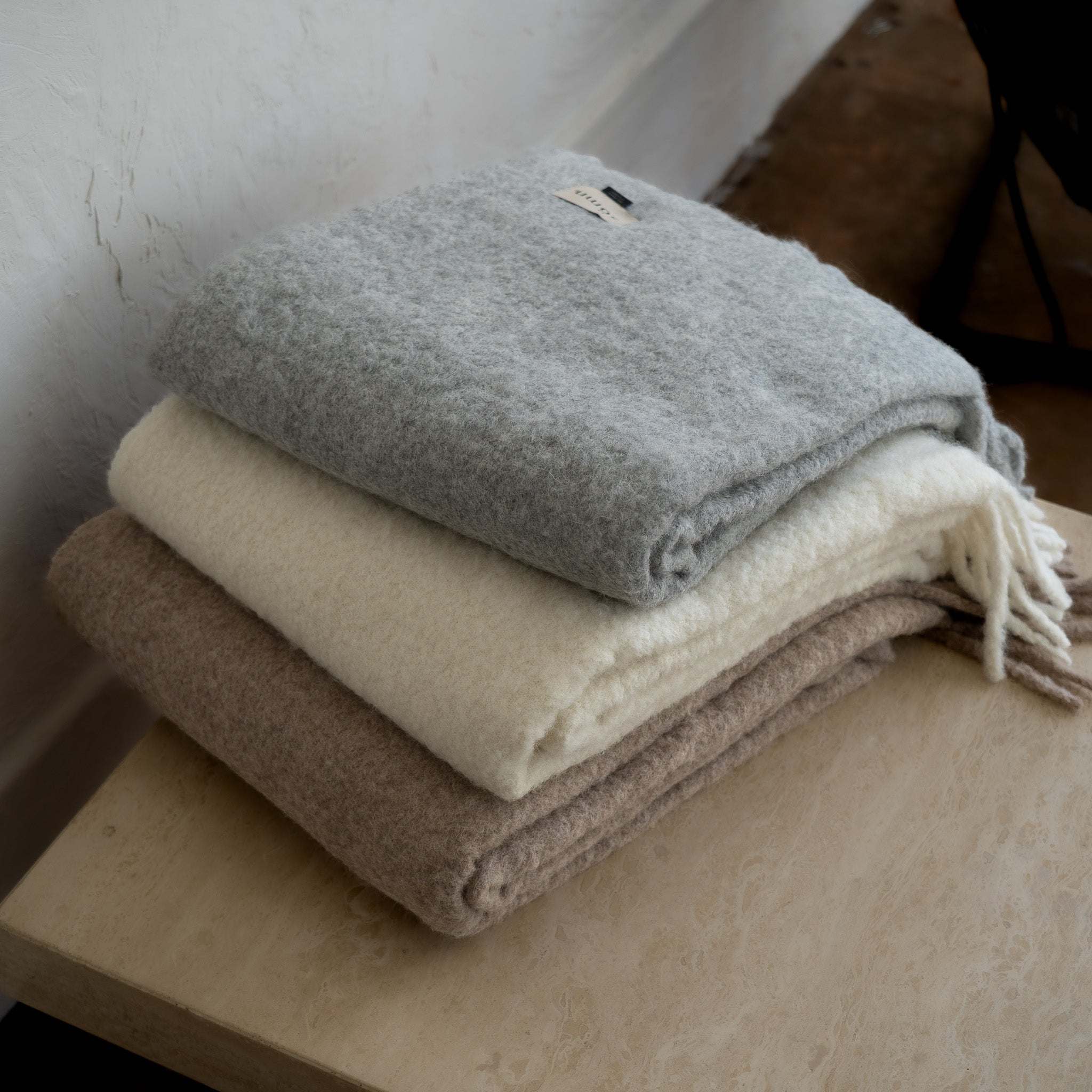 Stack of folded blankets in gray, beige, and brown on a wooden surface.