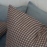 A close-up of a square throw pillow with a brown and beige diamond lattice pattern, resting on a sofa with blue-gray cushions in the background.