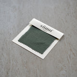 Olive Green fabric swatch in a 'somn' package on a gray surface