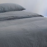 A close-up of a bed dressed in textured gray bedding, including a gray duvet cover and a matching gray pillow against a plain light background. #color_ocean-teal 