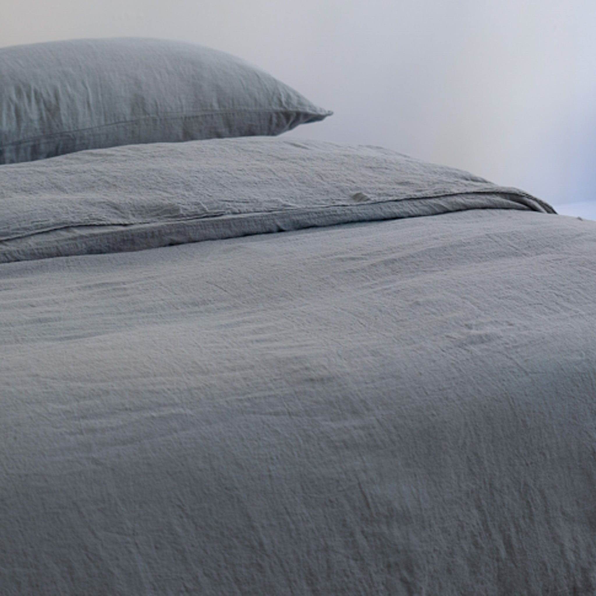 A close-up of a bed dressed in textured gray bedding, including a gray duvet cover and a matching gray pillow against a plain light background. #color_ocean-teal 