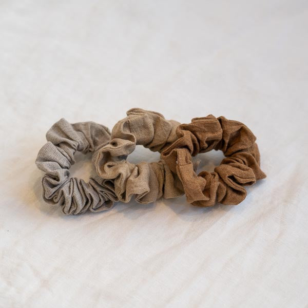 Three Somn Home Linen scrunchies of different colors on a white surface.