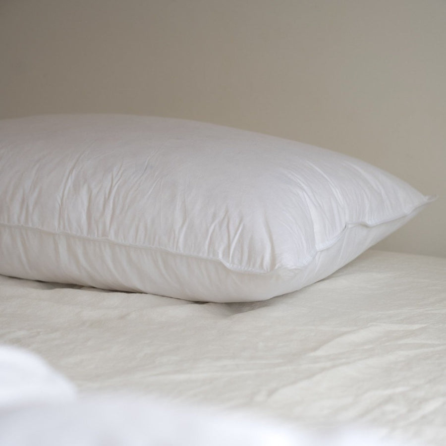 A close up of a white Somn Home luxury duck feather pillow insert cushion insert on a bed.